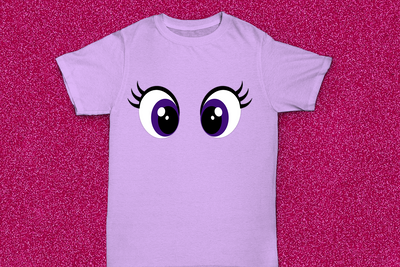 A lavender tee on a glittery hot pink background. The tee has large purple cartoon eyes.