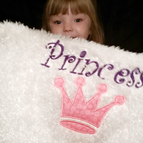 Princess crown applique on a pillow with a little white girl holding it.