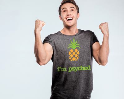 Excited happy white man with a dark grey shirt that has a pineapple design and says "I'm psyched."