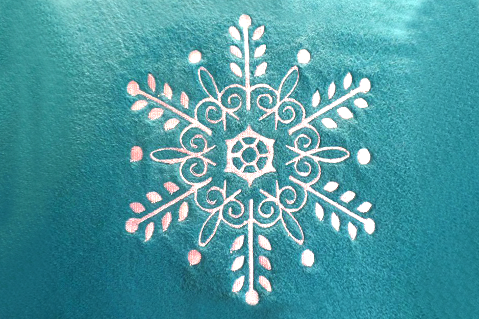 An intricate white snowflake embroidery on turquoise fleece fabric.