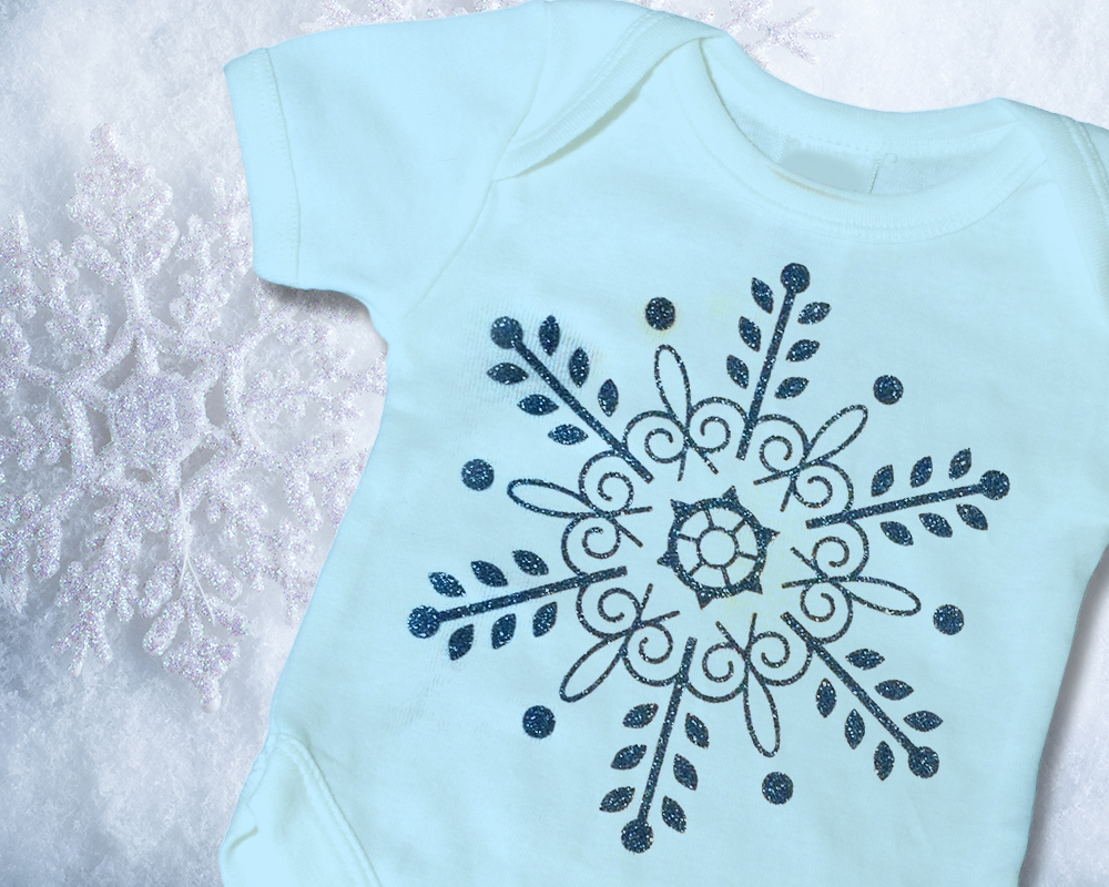 An intricate snowflake made of blue glitter vinyl on a pale blue baby onesie.