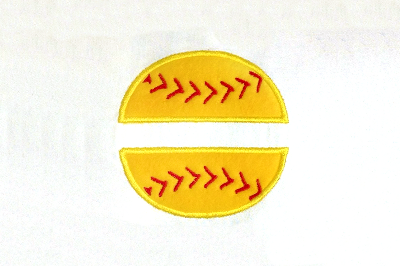 Embroidered onto a white piece of fabric is a yellow applique softball with red stitching and a split space in the middle.