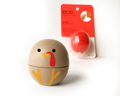 An EOS brand lip balm container in beige, decorated with a turkey face and turkey feet. An unopened EOS package is out of focus in the background.