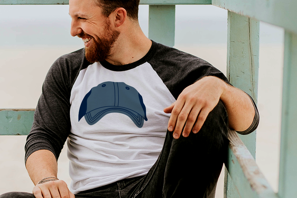 Bearded white person wearing a raglan tee with a design featuring a baseball cap