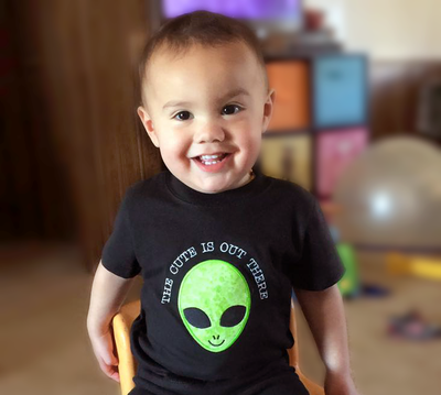 Asian baby with an applique alien on his shirt and the embroidered words "the cute is out there."
